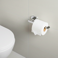 Toilet paper roll on a holder next to a toilet in a bathroom.