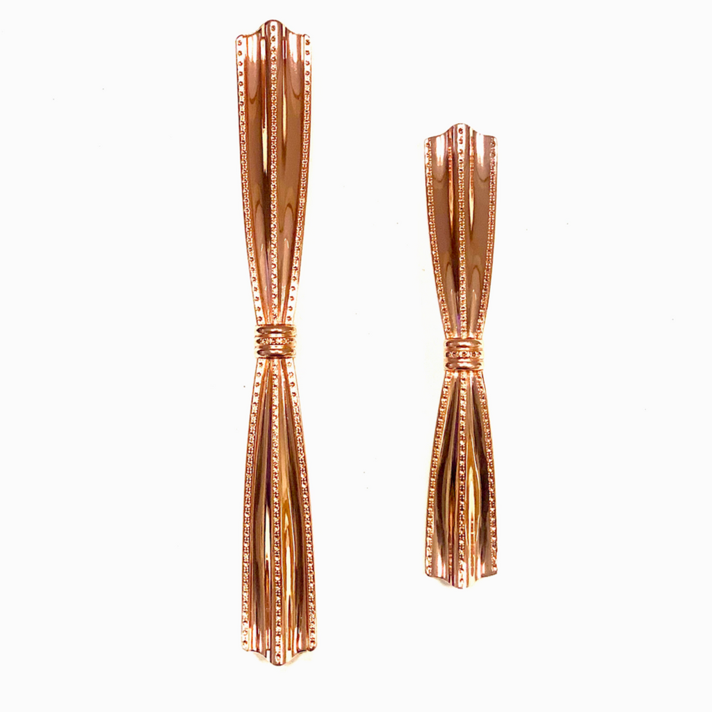 A pair of rose gold colored metal cabinet pulls with a ribbed design, displayed against a white background.