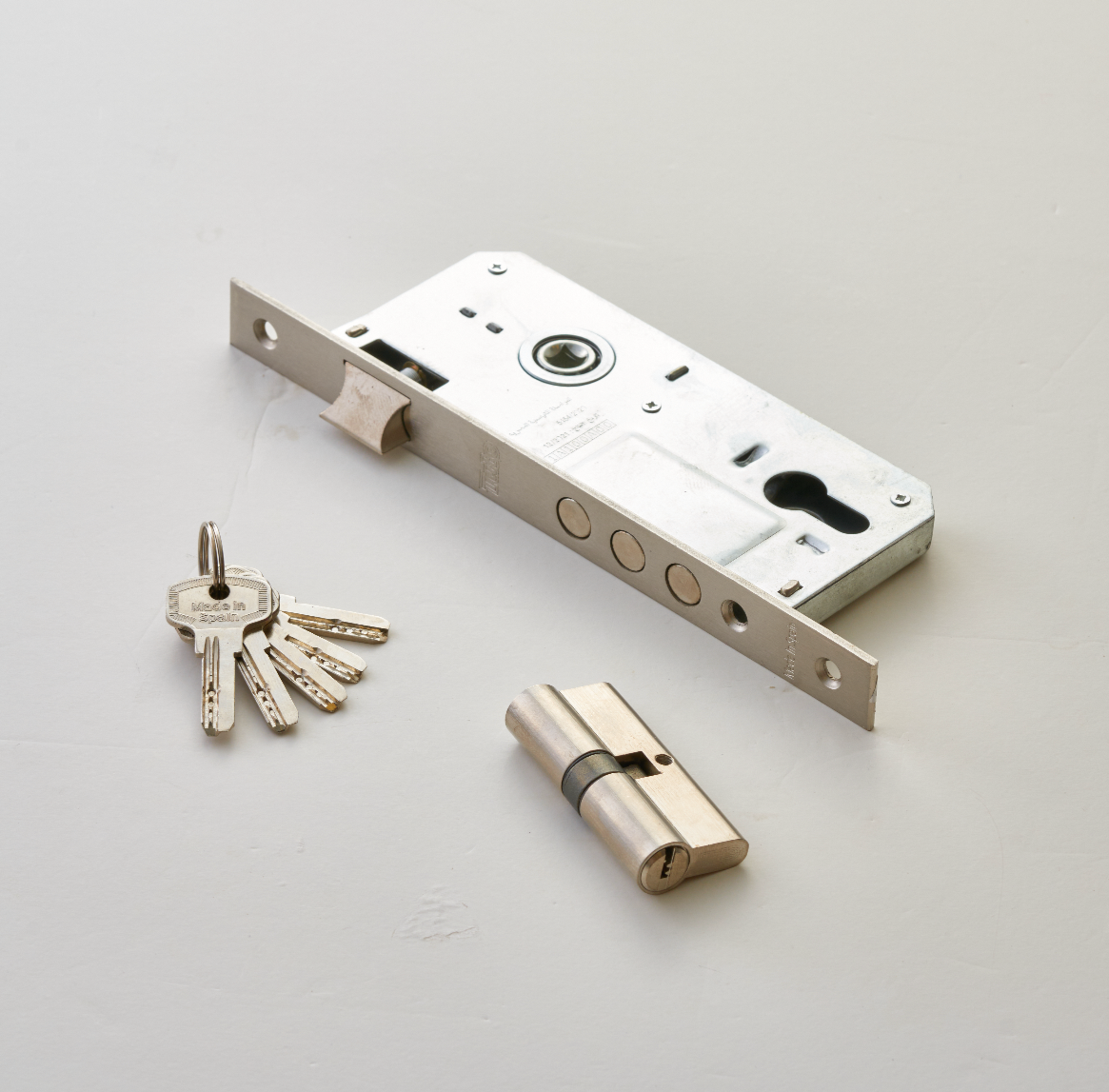 A silver computer door lock with a set of keys and a cylindrical lock component placed on a white surface.